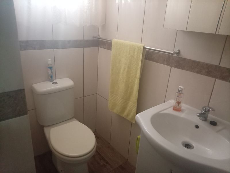 A compact bathroom featuring tiled walls, a standard toilet, a wall-mounted washbasin, and a medicine cabinet.