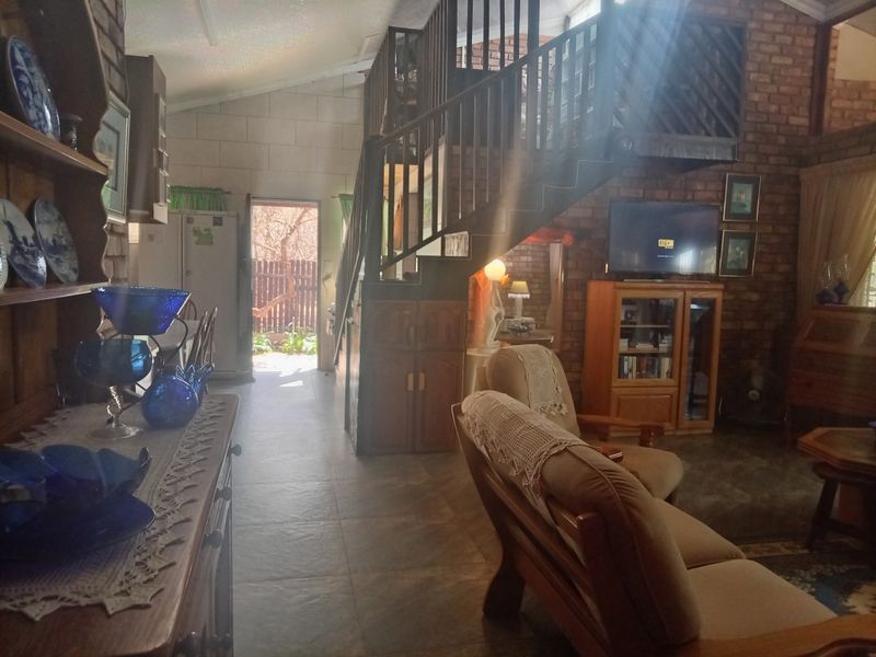 Spacious living area featuring exposed brick walls, vaulted ceilings, and a timber staircase leading to an upper level, with direct access to the exterior.