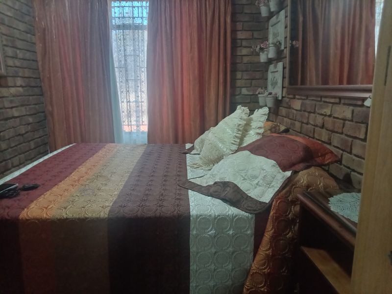 A bedroom featuring rustic exposed brick walls and a large window, providing a warm and textured aesthetic.