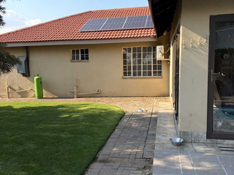 Rear exterior view of the house featuring a lawn, paved walkway, stone patio, and roof-mounted solar panels.