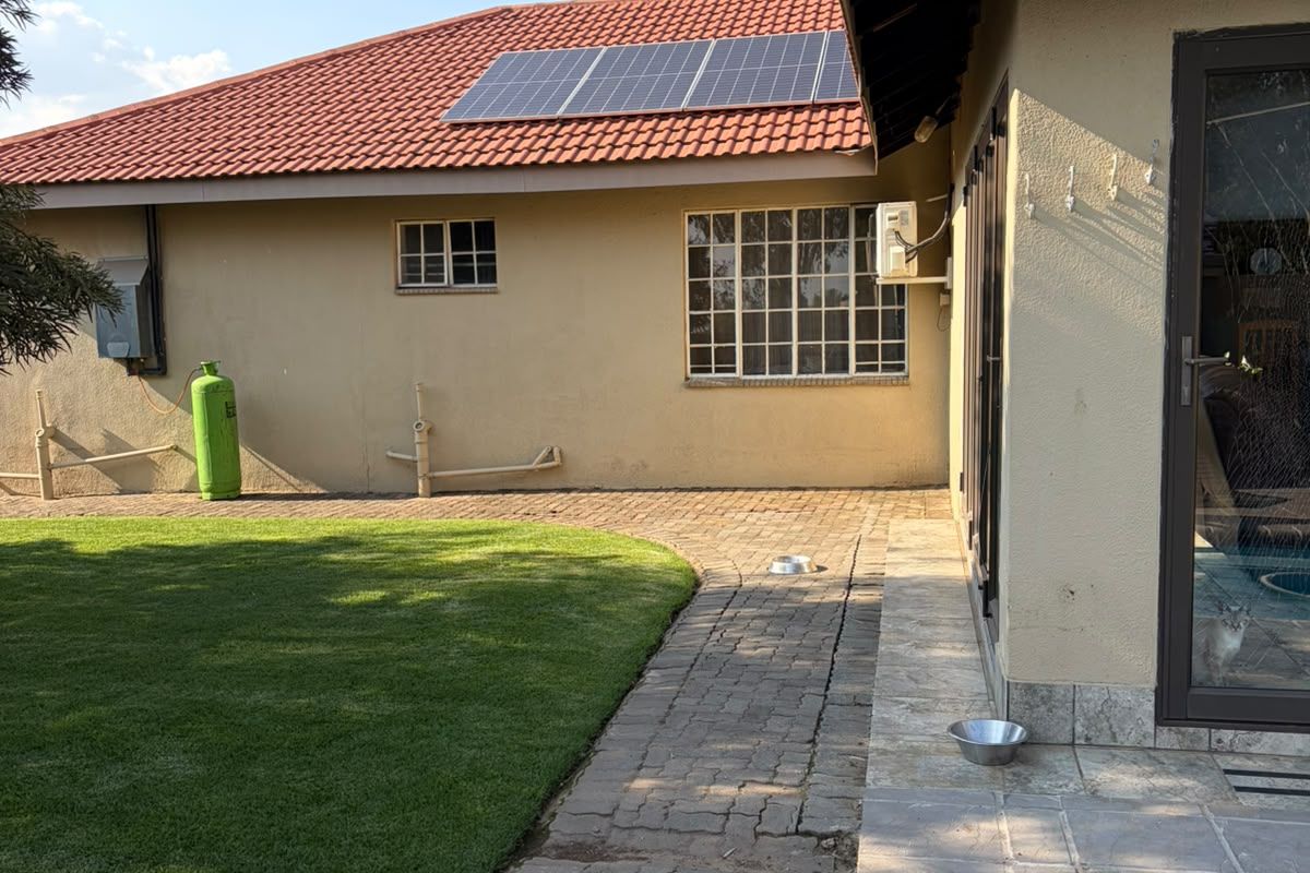 Rear exterior view of the house featuring a lawn, paved walkway, stone patio, and roof-mounted solar panels.