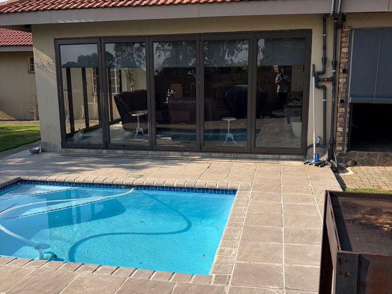 Outdoor pool area featuring a tiled deck, swimming pool, and folding glass doors leading into the main living space.