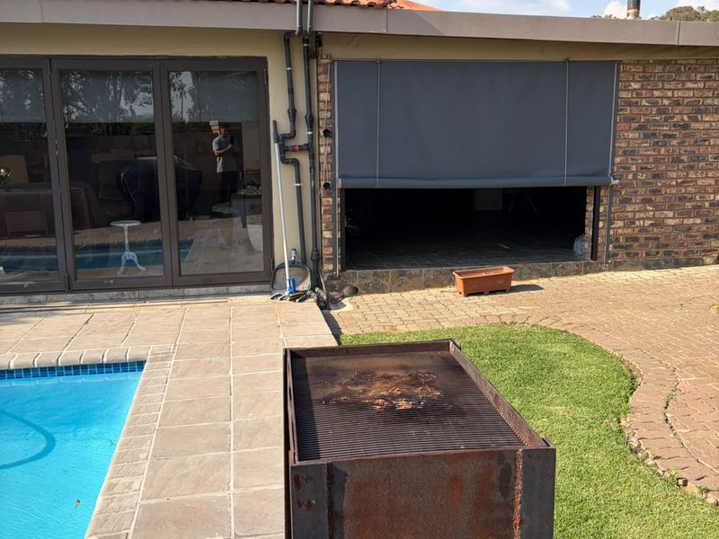 Outdoor pool area featuring a paved patio, brick exterior, sliding glass doors, and a covered patio section with a roller blind.