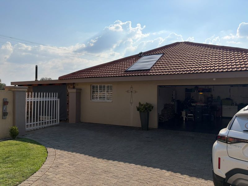 Front view of the property featuring a paved driveway, garage access, and a tiled roof equipped with a solar water heating panel.