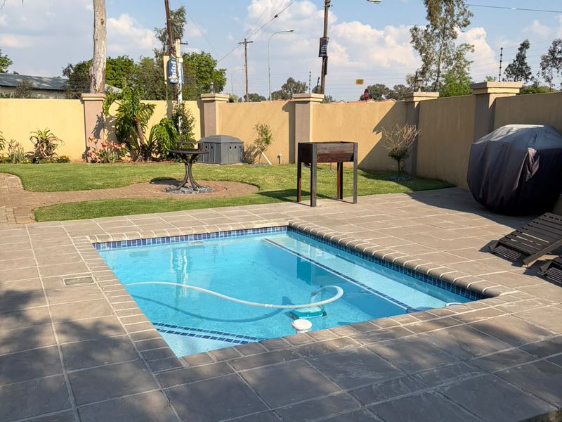 A well-maintained outdoor pool area featuring a paved deck, surrounding lawn, and a perimeter boundary wall, ideal for outdoor relaxation and entertainment.