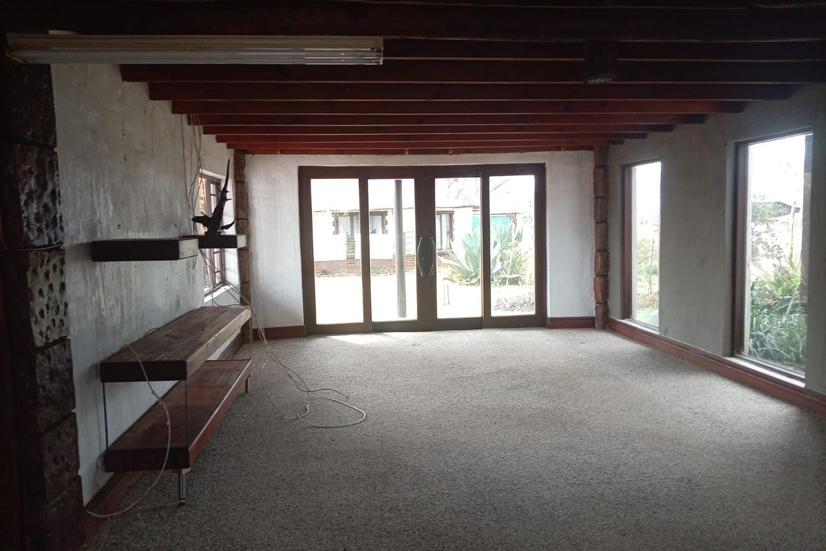 Spacious living area featuring exposed timber ceiling beams, large windows, and sliding glass doors leading to the garden, offering a blank canvas for renovation.