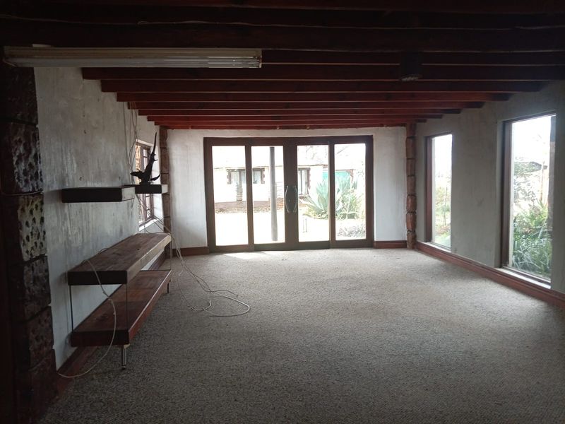 Spacious living area featuring exposed timber ceiling beams, large windows, and sliding glass doors leading to the garden, offering a blank canvas for renovation.