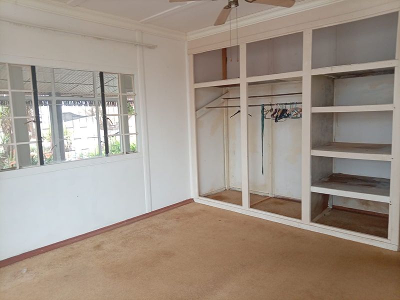 A vacant bedroom featuring built-in wardrobe storage, a ceiling fan, and large windows. The room requires cosmetic updates to the flooring and cabinetry.