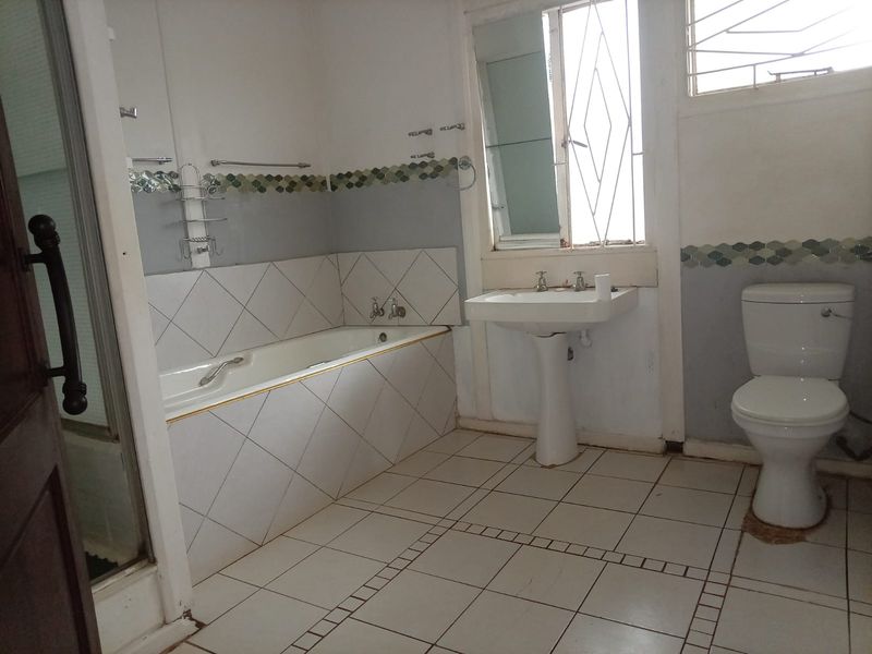 A functional bathroom featuring a bathtub, pedestal basin, and toilet, with tiled flooring and wall accents. The space is ready for cosmetic updates.