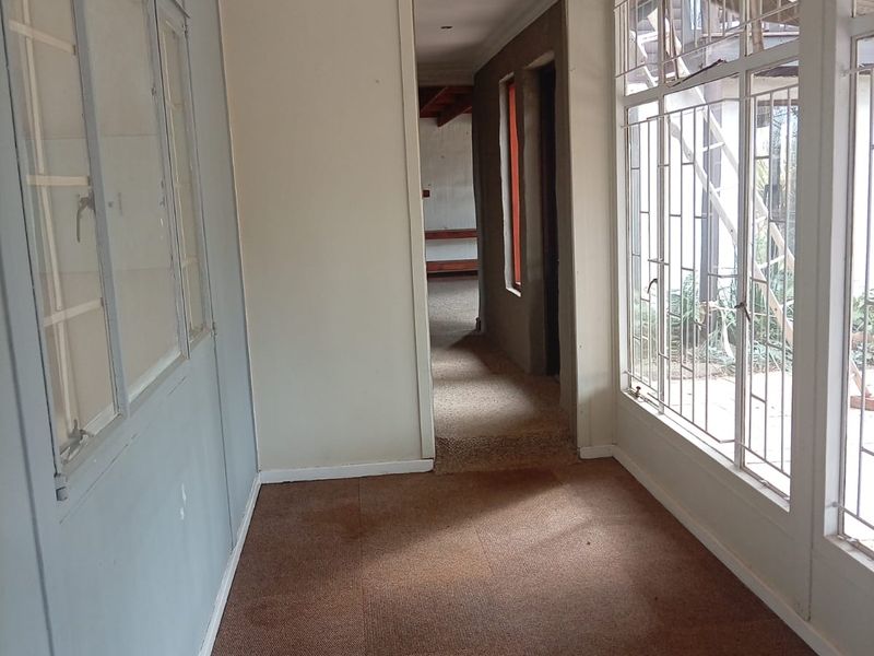 A vacant hallway featuring carpet flooring, large windows with security bars, and access to adjoining rooms.