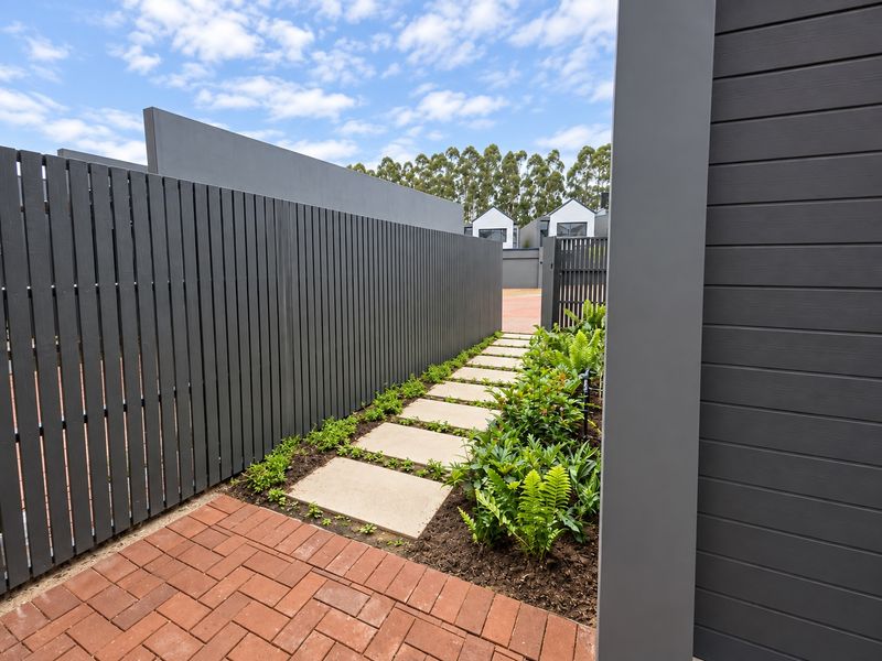 A modern entrance pathway featuring a concrete paver walkway, timber slat fencing, and neat garden beds leading towards the townhouse entrance.