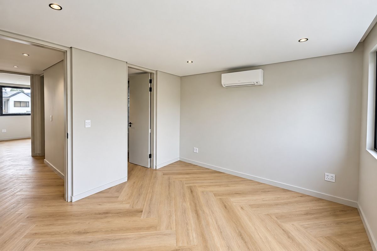 A bright, modern bedroom featuring high-quality herringbone vinyl flooring, recessed lighting, and a wall-mounted air conditioning unit.