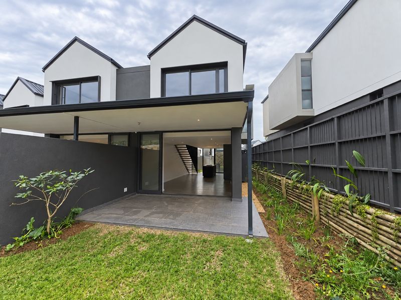 Rear view of a modern townhouse featuring a covered tiled patio, sliding glass doors, and a private garden with timber fencing.