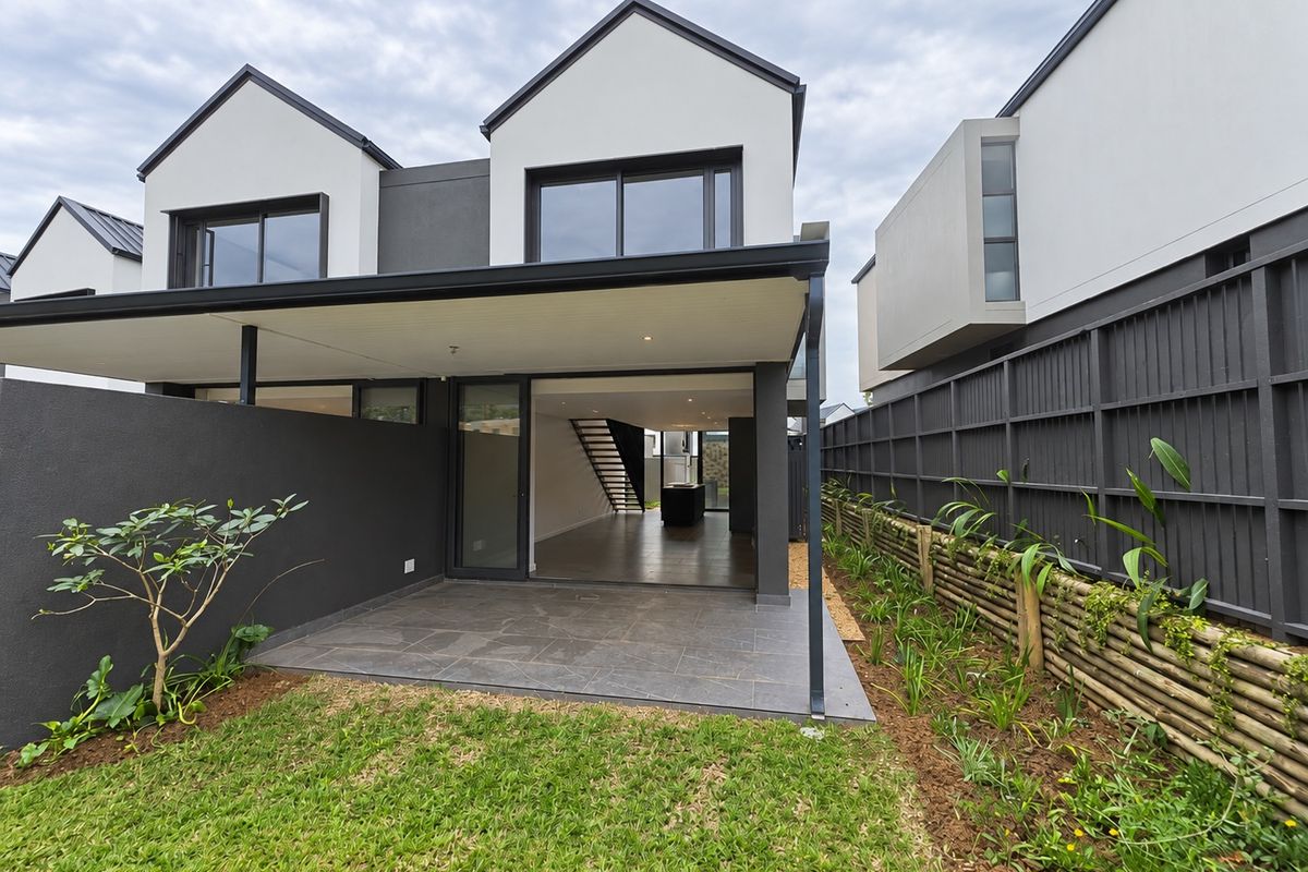Rear view of a modern townhouse featuring a covered tiled patio, sliding glass doors, and a private garden with timber fencing.