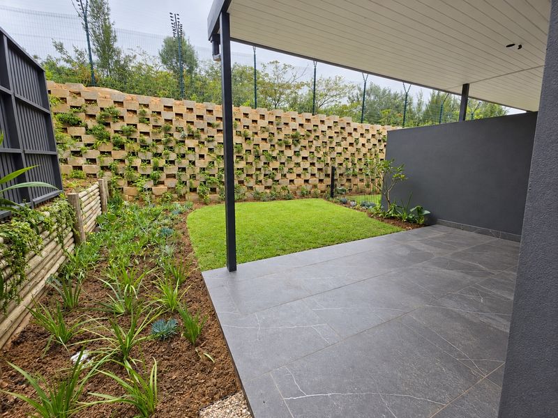 A modern covered patio featuring dark tiled flooring, overlooking a landscaped garden with a decorative retaining wall and secure electric fencing.