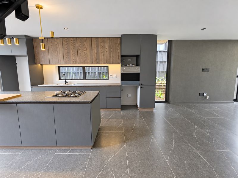 Modern open-plan kitchen featuring a central island with gas hob, sleek cabinetry, stone countertops, and large format floor tiles in a contemporary townhouse.