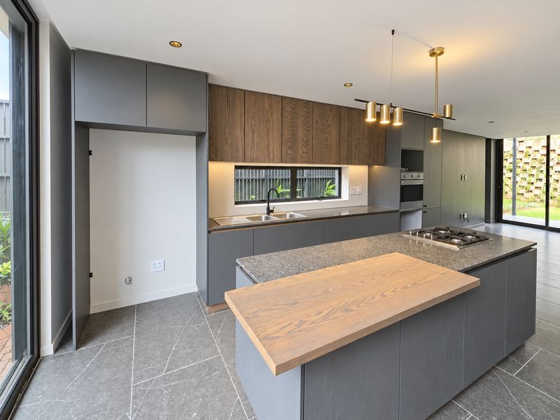Modern kitchen featuring a large island with stone countertops, built-in oven, gas cooktop, and high-quality cabinetry with integrated lighting.