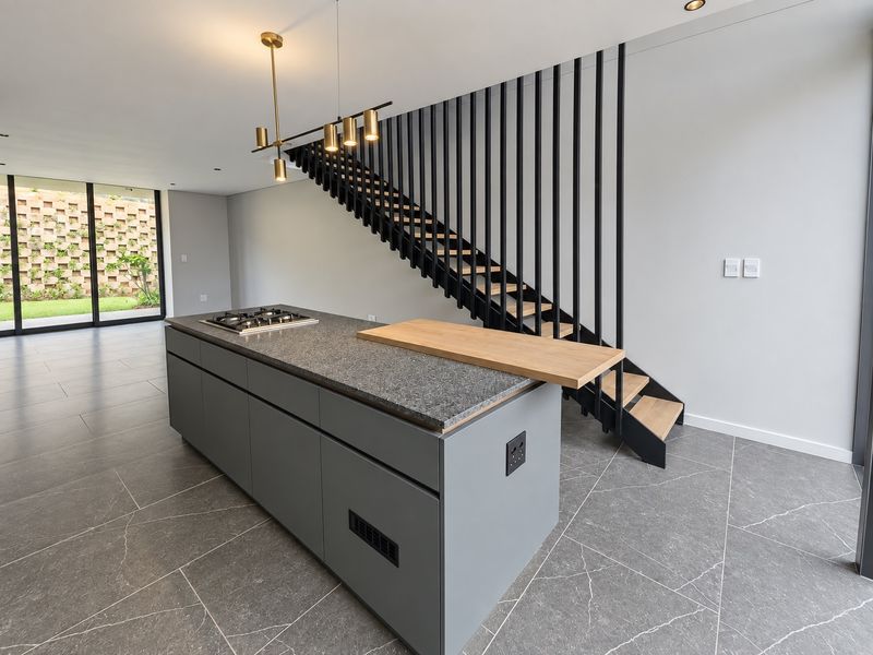 Modern open-plan living area featuring a sleek kitchen island with gas hob, contemporary staircase with metal balustrade, and large sliding doors to the garden.