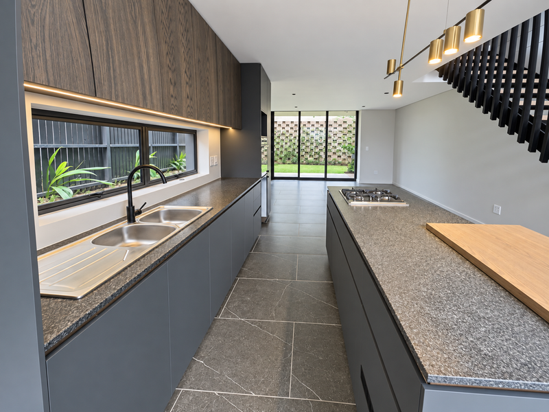 Modern open-plan kitchen featuring dark cabinetry, stone countertops, gas cooktop, and seamless flow to the rear patio through large sliding glass doors.