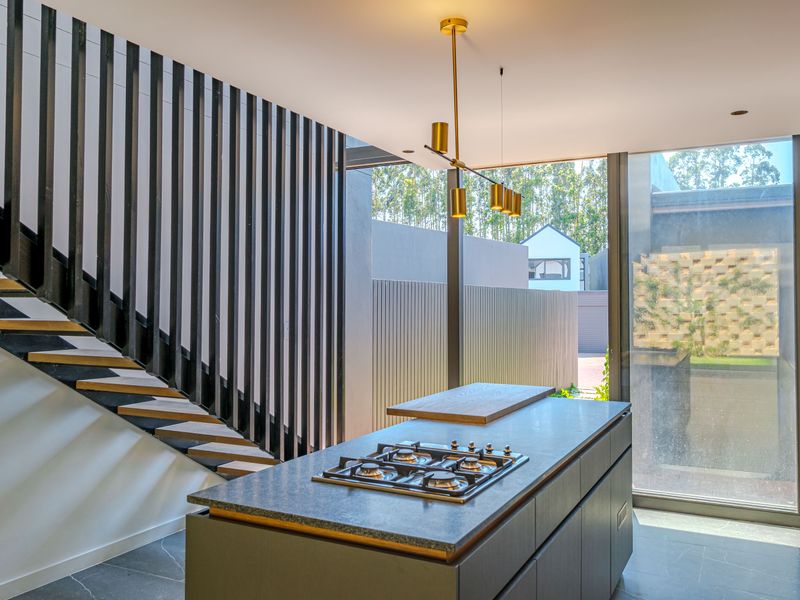 Modern kitchen featuring a central island with integrated gas hob, sleek cabinetry, and an adjacent architectural open-riser staircase with vertical slat detailing.