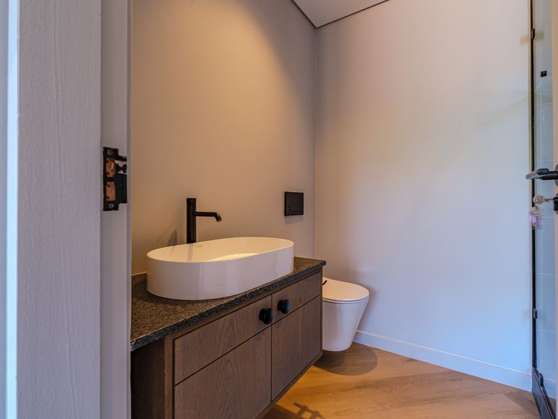 Modern bathroom featuring a vessel sink on a timber vanity, stone countertop, and wall-hung toilet with contemporary black fixtures.
