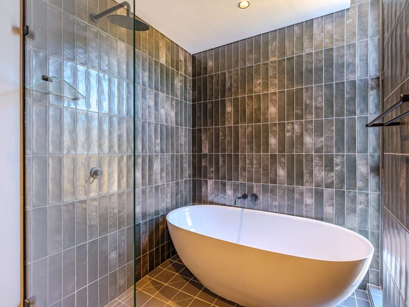Modern bathroom featuring a sleek freestanding bathtub, glass-enclosed rain shower, and contemporary dark textured wall tiling.