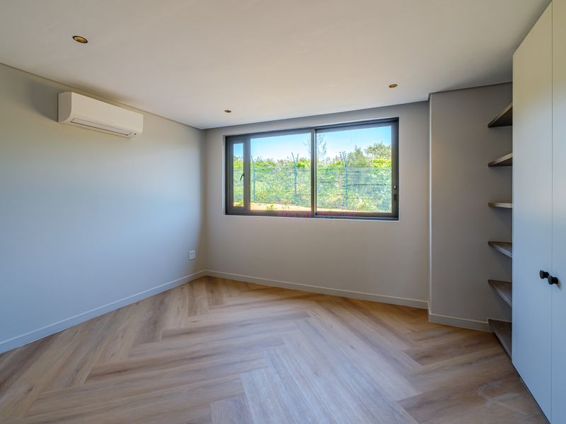 A bright, modern bedroom featuring herringbone wood flooring, built-in storage, and a split-system air conditioner, offering a clean and neutral living space.