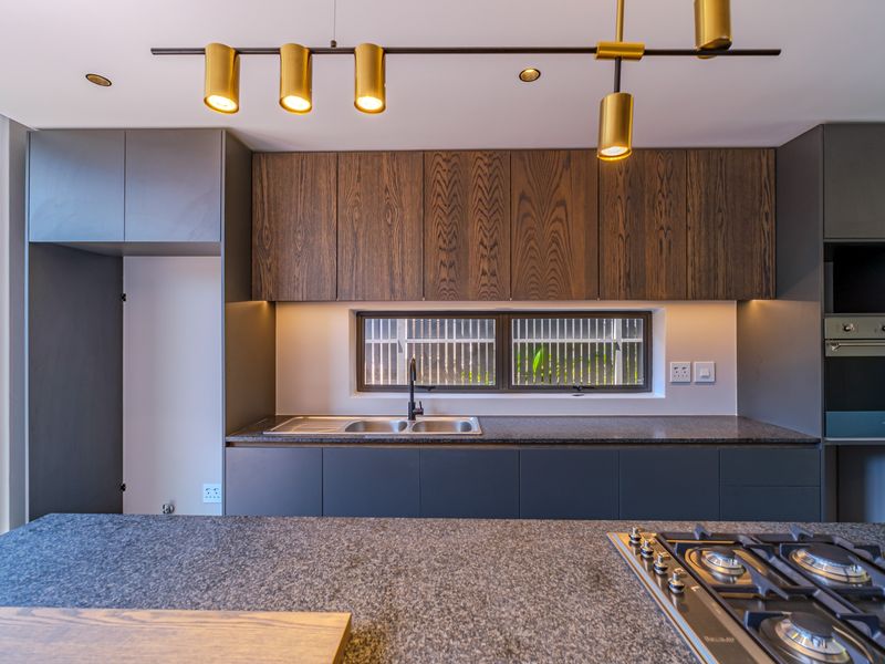 Modern kitchen featuring dark cabinetry, stone countertops, integrated gas hob, built-in oven, and stylish pendant lighting in a clean, contemporary design.