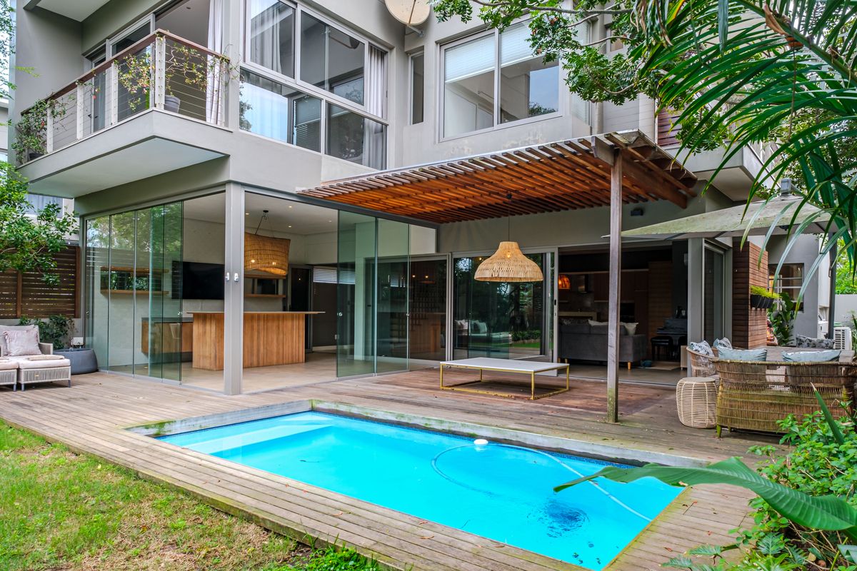 Rear exterior view of a modern townhouse featuring a swimming pool, timber decking, a wooden pergola, and seamless indoor-outdoor flow through glass sliding doors.