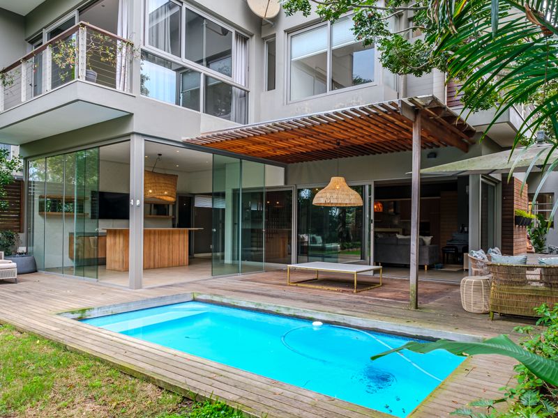 Rear exterior view of a modern townhouse featuring a swimming pool, timber decking, a wooden pergola, and seamless indoor-outdoor flow through glass sliding doors.
