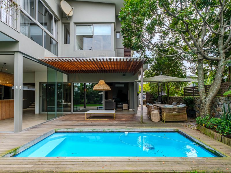 Outdoor pool area featuring timber decking, a wooden pergola, and seamless indoor-outdoor flow through large sliding glass doors.