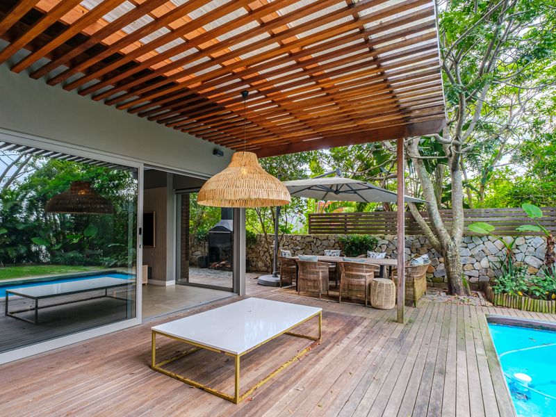 Spacious outdoor patio featuring timber decking, a pergola, and a swimming pool, seamlessly connected to the interior living space via large sliding glass doors.