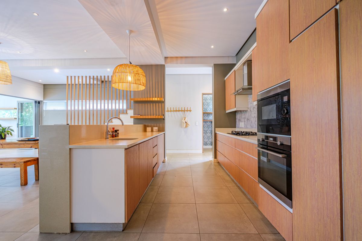 Modern kitchen featuring light wood cabinetry, stone countertops, integrated appliances, and a stylish timber slat divider, creating a seamless open-plan flow.