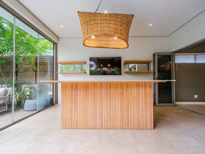 Modern indoor bar area featuring a slatted timber counter, floating shelves, and large glass sliding doors opening to an outdoor deck.