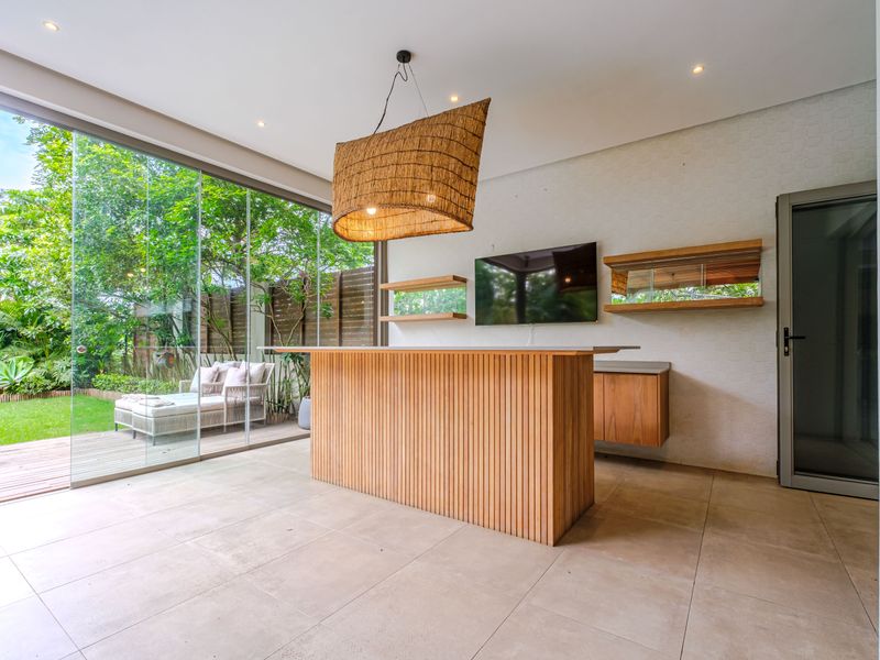 Modern covered patio featuring a built-in wooden bar, recessed lighting, and large sliding glass doors opening to a landscaped garden.