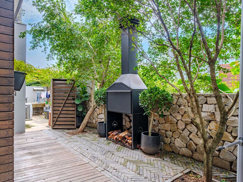 A private outdoor patio area featuring a built-in braai, timber decking, and a decorative stone wall, perfect for outdoor entertaining.