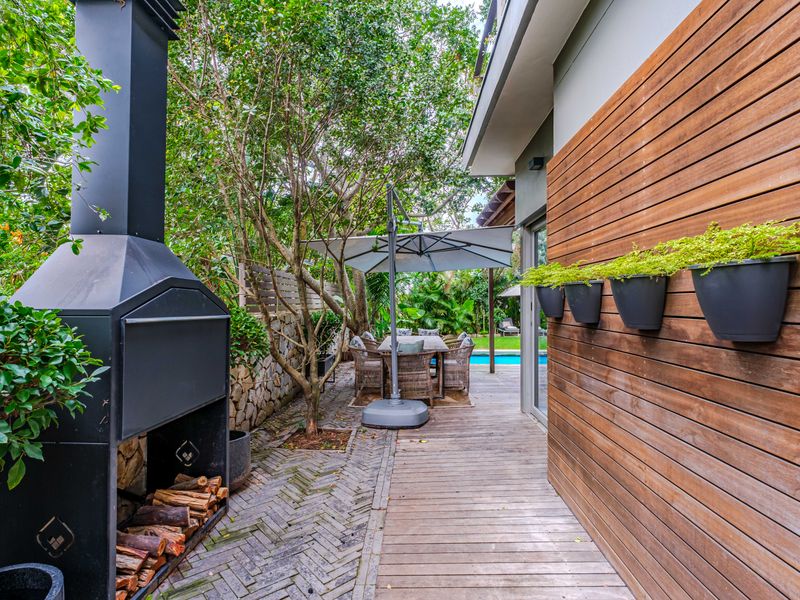 A well-maintained outdoor patio featuring timber decking, herringbone brick paving, and a built-in fireplace, creating an inviting space for outdoor entertaining.