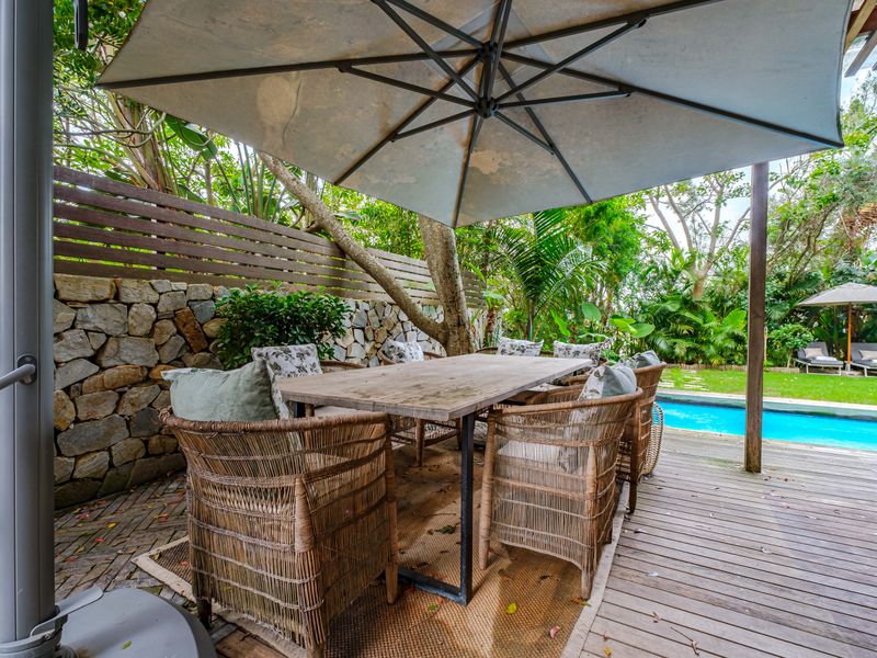 A covered outdoor patio area featuring timber decking, a stone retaining wall, and direct access to a private swimming pool.