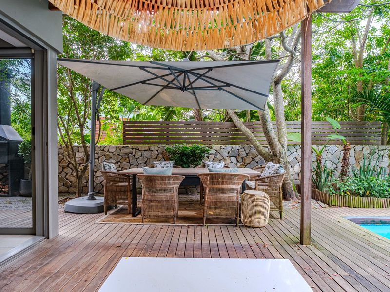 Covered timber deck patio featuring a built-in fireplace, stone retaining wall, and direct access to a swimming pool in a landscaped garden setting.