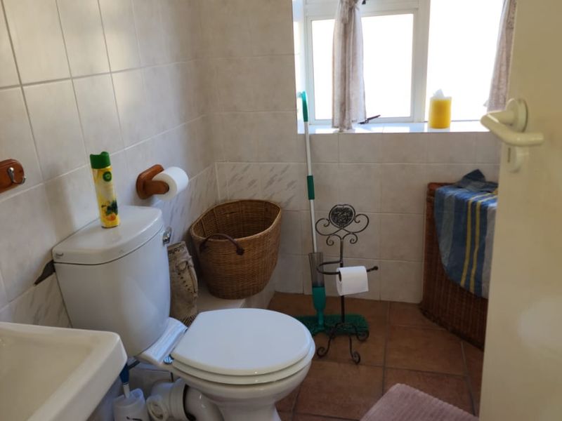 A functional bathroom featuring tiled walls and flooring, a standard toilet, and a washbasin, with natural light provided by a window.