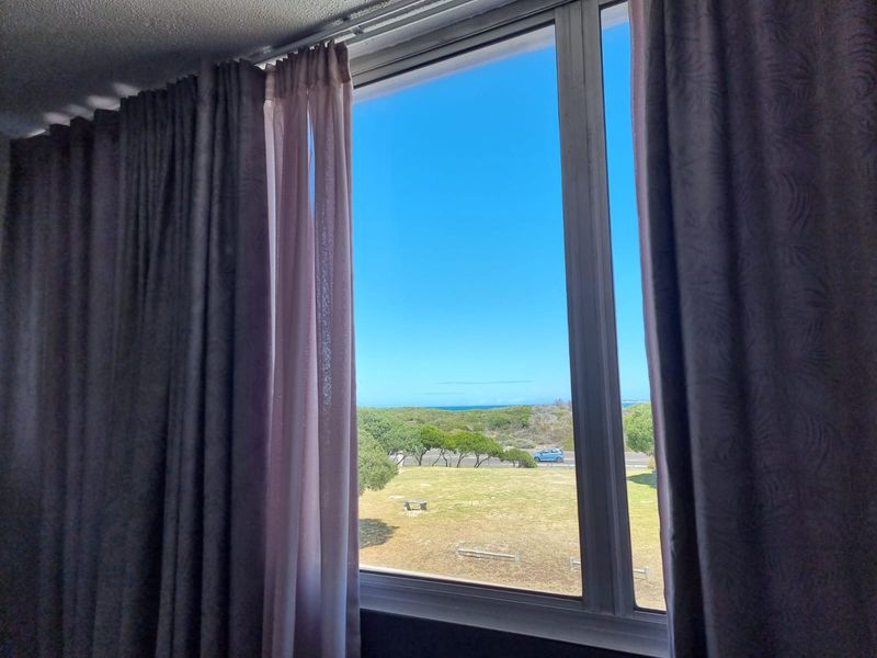 A view through a large window overlooking a coastal landscape with green space and distant ocean horizon.