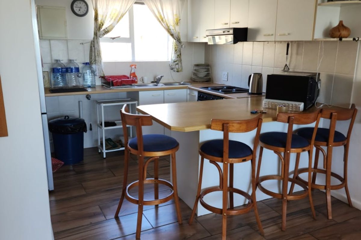 A functional kitchen featuring white cabinetry, a breakfast bar, tiled backsplash, and wood-look tiled flooring, providing a practical and well-lit cooking and dining space.