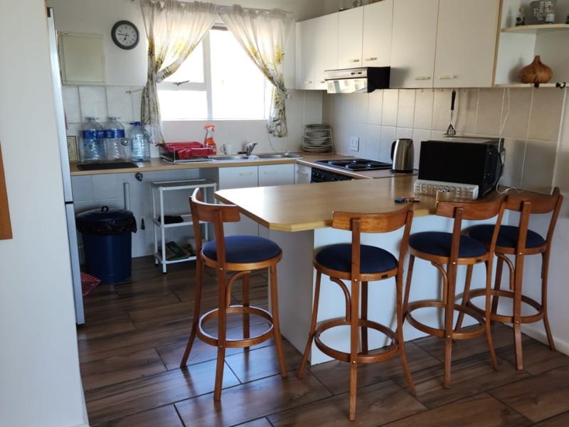 A functional kitchen featuring white cabinetry, a breakfast bar, tiled backsplash, and wood-look tiled flooring, providing a practical and well-lit cooking and dining space.