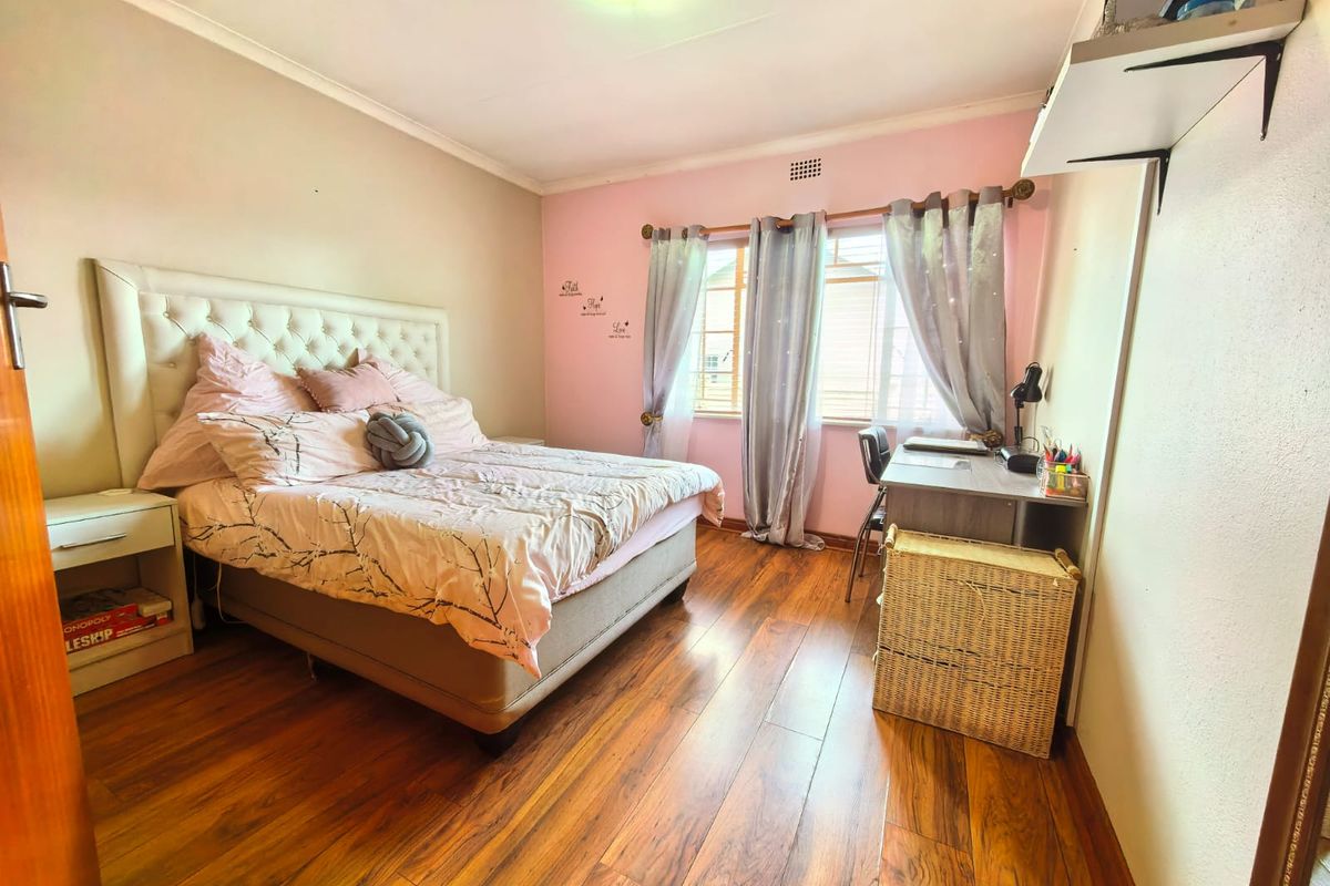 A bedroom featuring warm-toned laminate flooring, a large window with curtain rod, and a wall-mounted shelf.