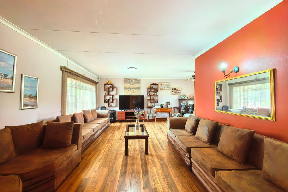 Spacious living room featuring warm-toned laminate flooring, a coved ceiling, and a prominent accent wall with a decorative mirror.