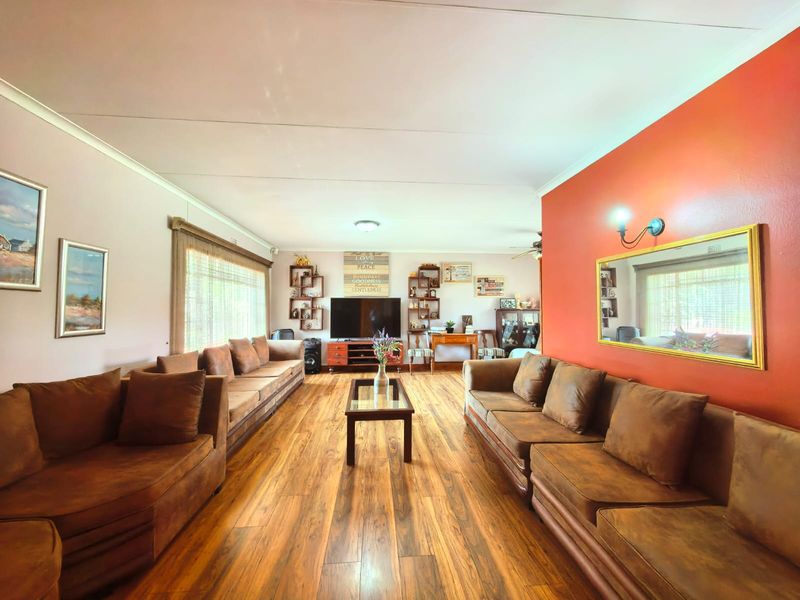 Spacious living room featuring warm-toned laminate flooring, a coved ceiling, and a prominent accent wall with a decorative mirror.