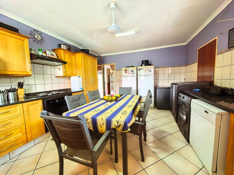 Open-plan kitchen and dining area featuring wooden cabinetry, granite countertops, tiled flooring, and integrated appliance spaces.