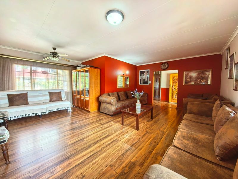 Spacious living room featuring warm-toned laminate flooring, a ceiling fan, and bold red accent walls, providing a comfortable and inviting atmosphere.