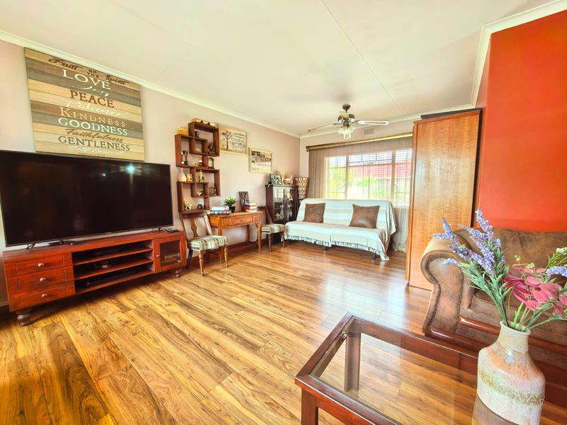 A spacious living room featuring warm-toned laminate flooring, a ceiling fan, and natural light from a large window.