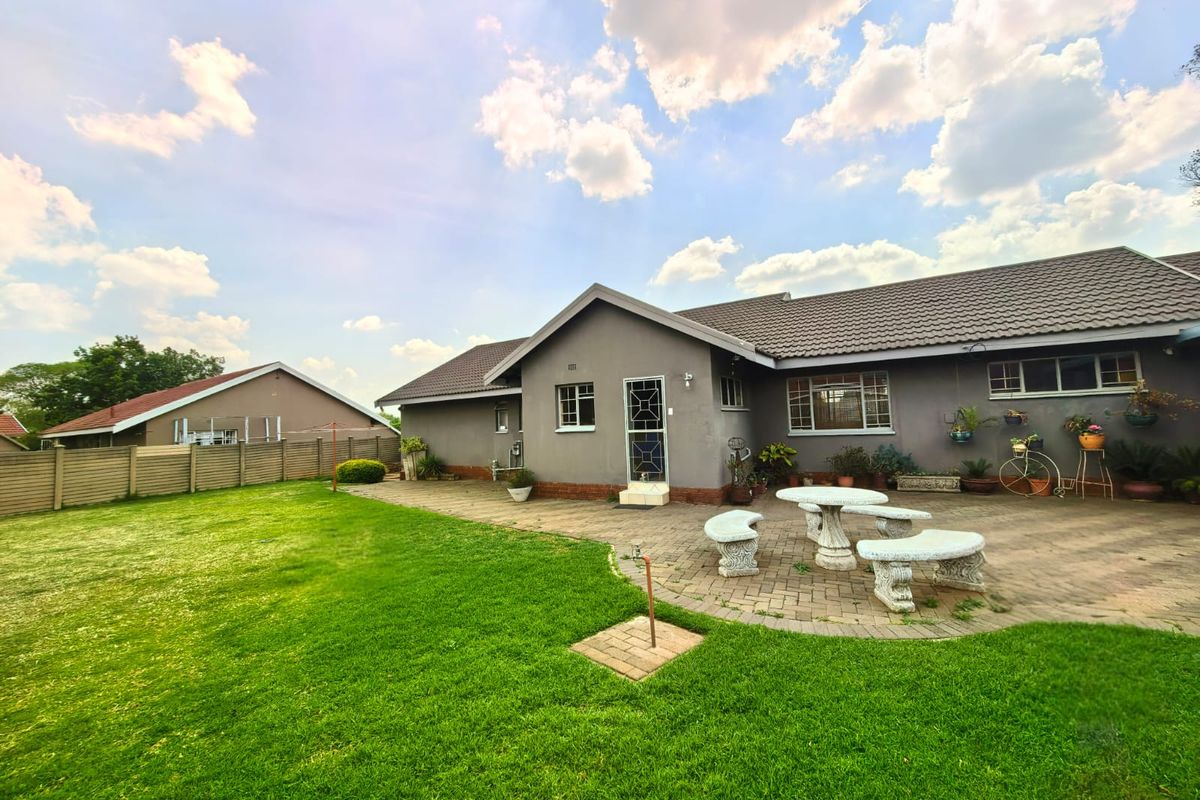 Rear view of the property featuring a paved patio area, well-maintained lawn, and perimeter fencing under a clear sky.